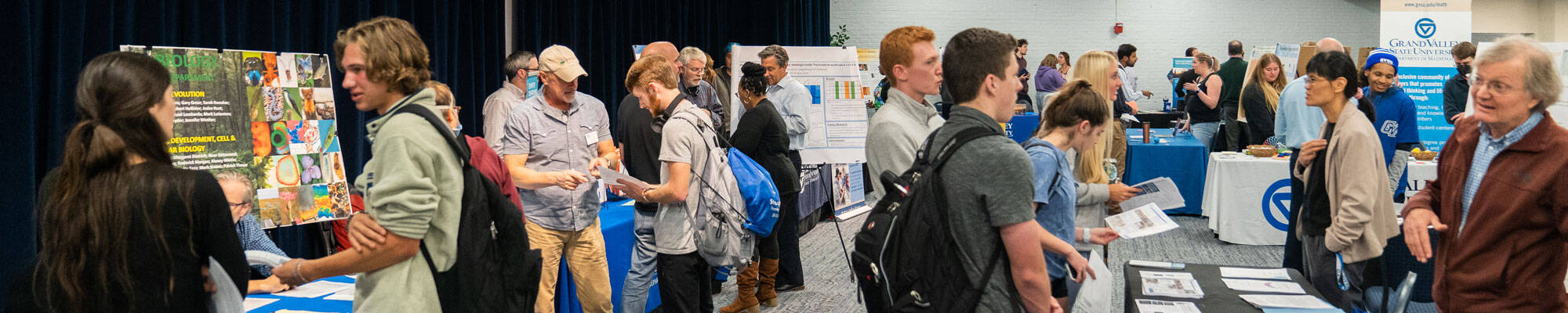 Student at the Undergraduate Research Fair exploring the different tables and talking with faculty